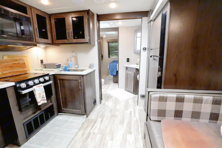 RV rental interior features a functional kitchen with stove, microwave, sink, leading to a bedroom/bath. Light wood flooring & dinette.. Grand Design Transcend Xplor 2022
