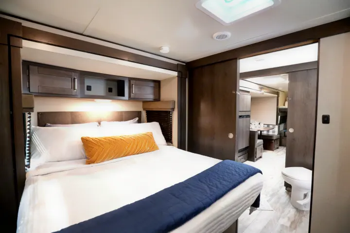 Spacious RV rental bedroom with cozy bed, overhead storage, and sliding door to the living area and bathroom.. Grand Design Transcend Xplor 2022