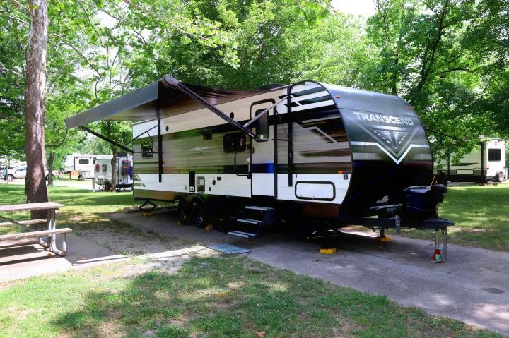 A Transcend RV rental parked at a lush, shady campsite, perfect for a peaceful travel trailer getaway.. Grand Design Transcend Xplor 2022