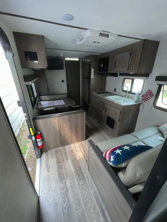 Inside an RV rental: a fully equipped kitchen, dining area, and cozy seating. Modern interior with light wood tones and amenities.. Gulf Stream Ameri-Lite 2022