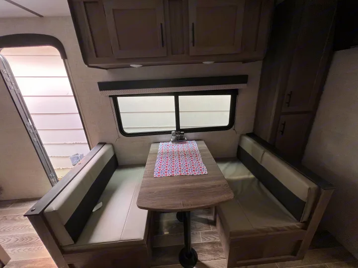 RV rental dinette showing comfortable booth seating, a table with a festive cloth, and windows for natural light.. Gulf Stream Ameri-Lite 2022