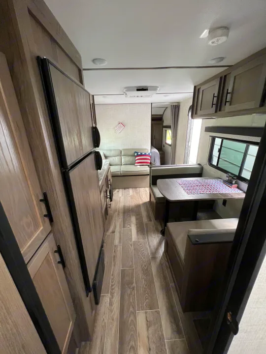 View of an RV rental interior: modern living area, dining booth with red, white, and blue runner, and kitchen.. Gulf Stream Ameri-Lite 2022