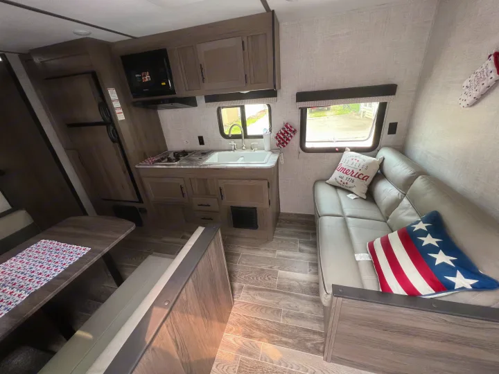 RV rental interior: Modern kitchen, dining booth, and sofa with wood-look flooring. Perfect for travel.. Gulf Stream Ameri-Lite 2022
