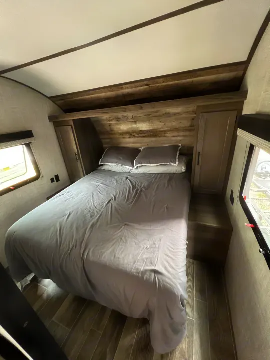This RV rental bedroom features a comfy bed, rustic wooden headboard, storage, and natural light.. Gulf Stream Ameri-Lite 2022