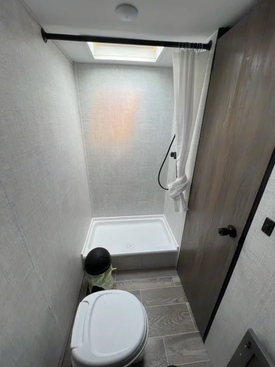 RV rental bathroom, featuring a compact shower, toilet, and modern interior finishes like textured walls and tiled floor.. Gulf Stream Ameri-Lite 2022