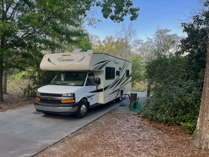 A white Coachmen Freelander RV rental is parked at a scenic, tree-lined campsite with utility hookups.. Coachmen Freelander 27QB 2020