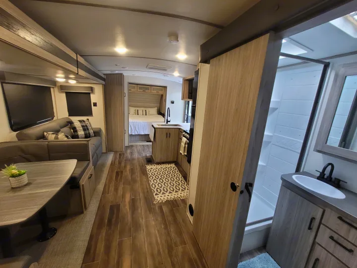 Step inside this bright RV rental, showcasing a full bathroom, stylish living area with dining, and a cozy bedroom section.. Keystone Passport 2022