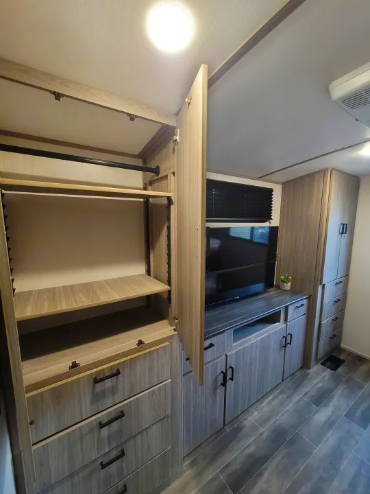 Spacious RV rental storage: open light wood wardrobe, shelves, and hanging rod, with TV and more cabinets visible.. Keystone Passport 2022