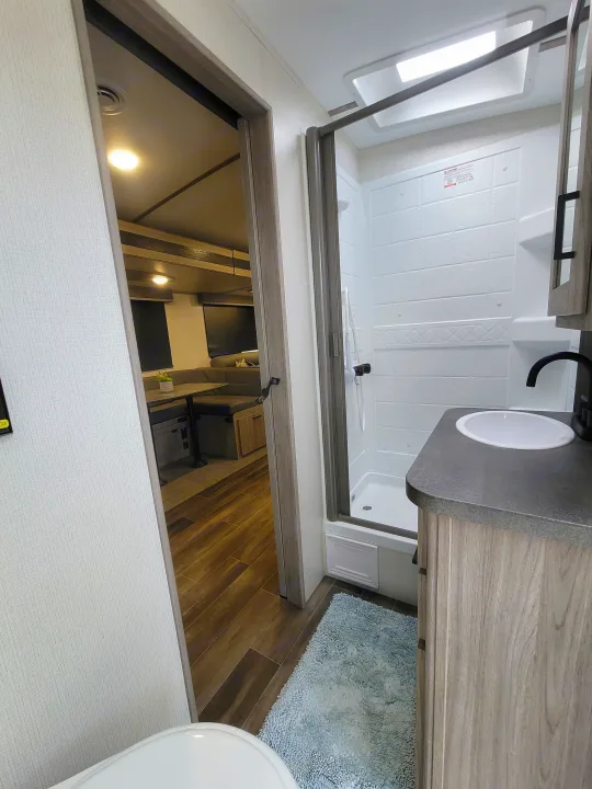 Explore this RV rental's modern bathroom with a full shower, sleek sink vanity, and warm wood flooring. Connects to living space.. Keystone Passport 2022