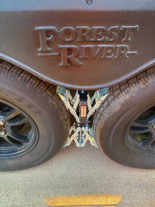 Close-up of an RV rental showing dual wheels, a MAXCHOCK wheel chock, and "FOREST RIVER" branding.. Forest River Surveyor Legend 2022