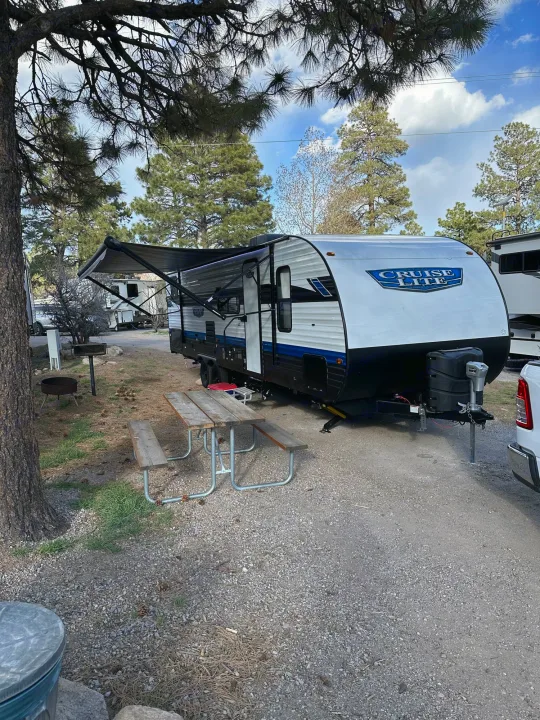 White & blue RV rental at a shaded campsite with a picnic table & fire pit, ready for outdoor adventures.. Forest River Salem Cruise Lite T282QXBL 2023
