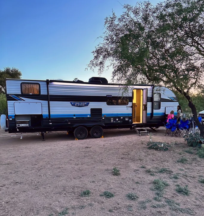 An RV rental travel trailer is set up at a dusty campsite with its door open and people gathered outside at dusk.. Forest River Salem Cruise Lite T282QXBL 2023