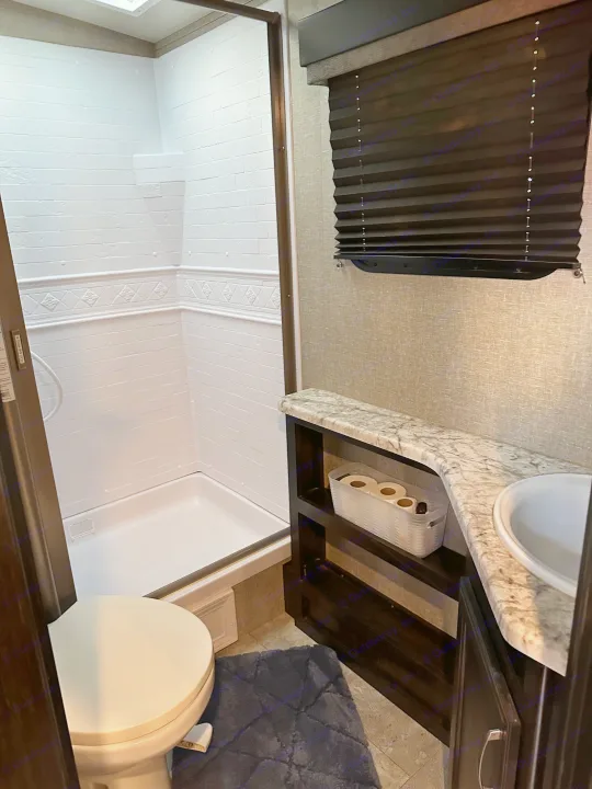 RV rental bathroom featuring a compact shower, toilet, and vanity with sink and storage, designed for efficient use of space.. Grand Design Imagine 2020