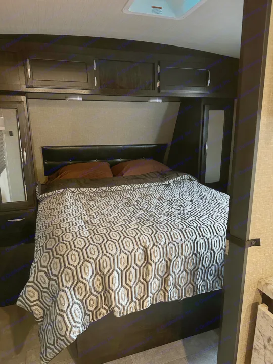 Cozy RV rental bedroom with dark wood built-in cabinets, a geometric patterned comforter, and compact design.. Grand Design Imagine 2020