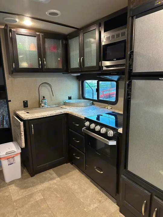 Spacious RV rental kitchen with dark cabinets, marble counters, and modern appliances including a Furrion oven and High Pointe microwave.. Grand Design Imagine 2020