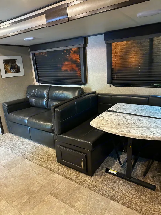 Experience this RV rental's inviting living area with a black leather sofa & dinette, stone-look table, and blinds.. Grand Design Imagine 2020