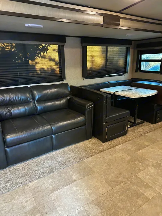 RV rental living area with a dark leather sofa, U-shaped dinette, and bright windows.. Grand Design Imagine 2020
