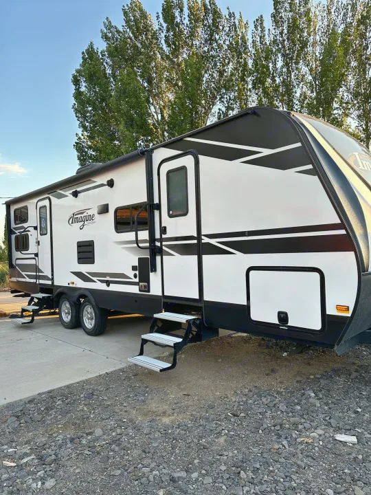 White and black "Imagine" travel trailer, ideal for an rv rental, parked on concrete.. Grand Design Imagine 2020