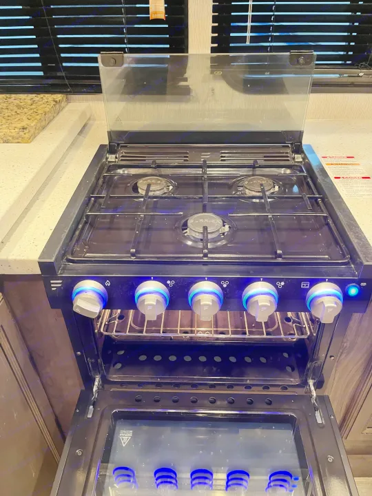Brightly lit RV stove/oven in an RV rental kitchen, featuring blue LED knobs & open door for inspection.. Heartland Torque 2020