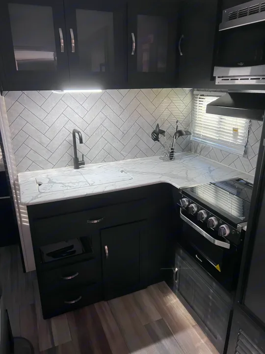 Modern rv rental kitchen with black cabinets, white marble-look counters, and a stylish herringbone backsplash.. Coachmen freedom express 287bhds 2022