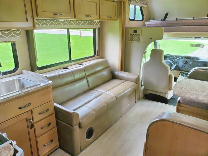 Inside a comfortable RV rental: light brown sofa, kitchen area with sink, dinette, and over-cab bunk bed. Wood-look flooring.. Thor Motor Coach Daybreak 30D 2020
