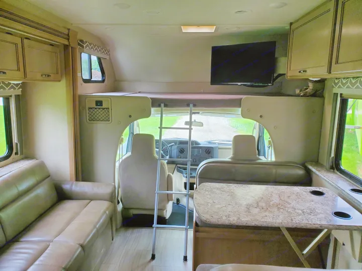 View inside an RV rental showing dinette, couch, bunk bed with ladder, and TV. Cozy travel setup.. Thor Motor Coach Daybreak 30D 2020