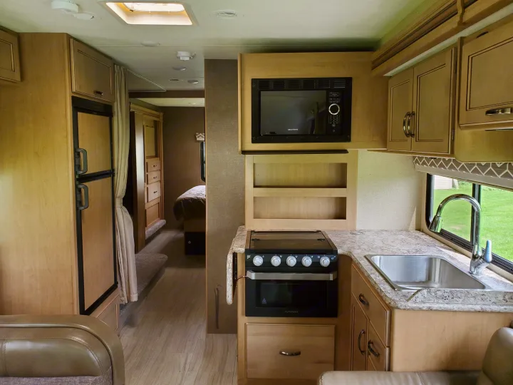RV rental kitchen: light wood cabinets, microwave, stove, sink, fridge. Bedroom visible beyond. Bright interior.. Thor Motor Coach Daybreak 30D 2020