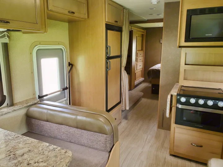 Bright RV rental interior with a full kitchen (oven, microwave), dinette seating, and a hallway leading to the bedroom area.. Thor Motor Coach Daybreak 30D 2020