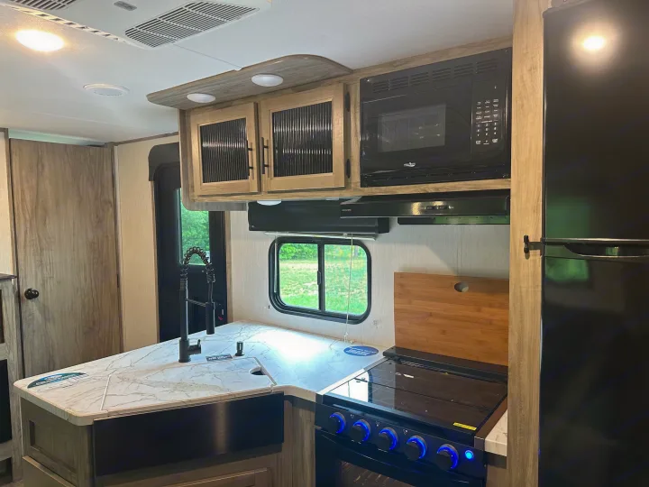 This modern RV rental kitchen features an island sink, stove, microwave, fridge, and light wood cabinets, creating a bright, functional space.. Forest River Cherokee Alpha Wolf 2022