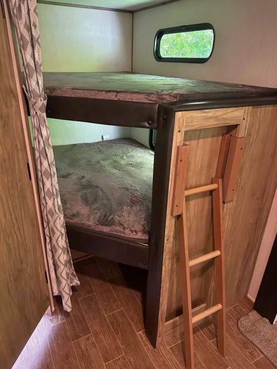 Cozy bunk beds in an RV rental, complete with a privacy curtain, window, and ladder for accessibility. Ideal for families.. Forest River Cherokee Alpha Wolf 2022