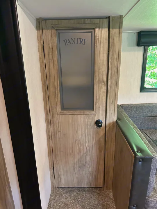 RV rental: Light wood-grain pantry door with frosted "PANTRY" glass, inside a travel trailer. Carpeted floor visible.. Forest River Cherokee Alpha Wolf 2022