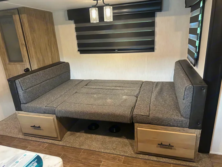 RV rental dinette converts to a bed, featuring storage drawers, modern lights, and blinds in a spacious interior.. Forest River Cherokee Alpha Wolf 2022