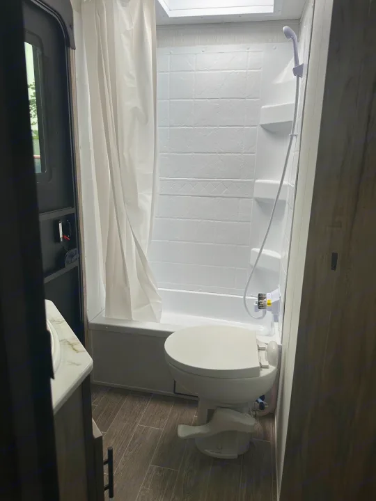 Clean RV rental bathroom with a white toilet, compact shower-tub combo, and a shower curtain. Ready for adventure!. Forest River Cherokee Alpha Wolf 2022