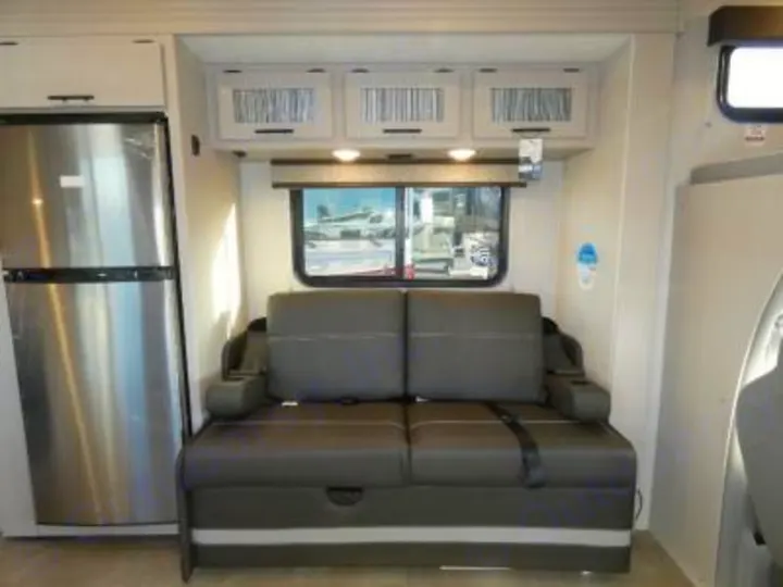 This RV rental's living space features a stainless steel fridge, a gray sofa, and overhead storage. Perfect for road trips.. Coachmen Freelander 29KB 2023