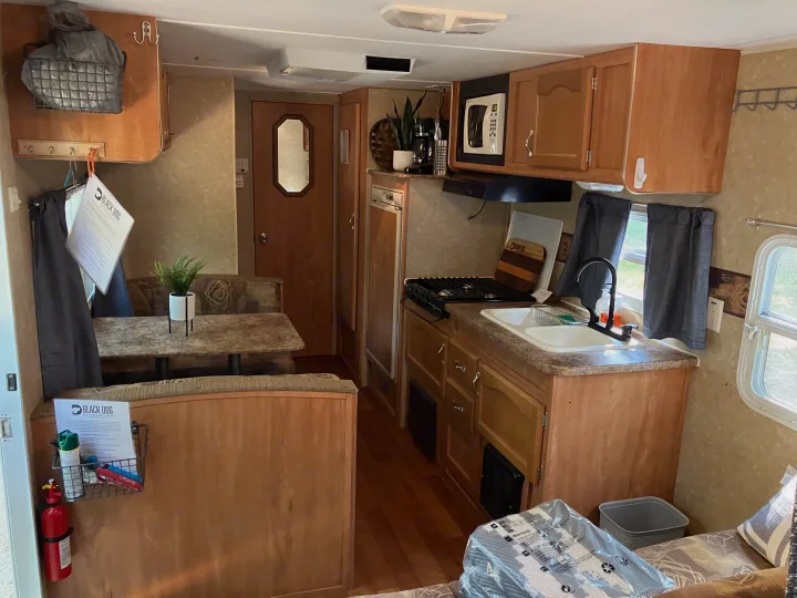 A clean RV rental interior with a compact kitchen (sink, stovetop, microwave) and a dining area with booth seating.. Gulf Stream Ameri-Lite 25 BS 2008