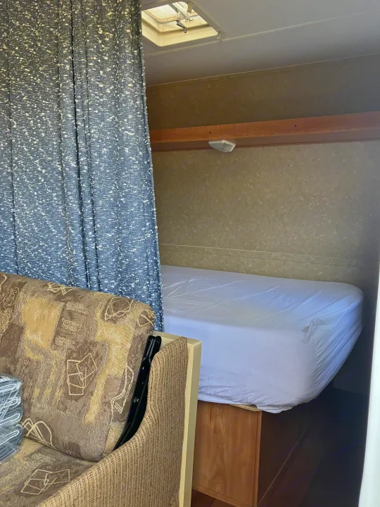 Cozy RV rental interior featuring a bed with white sheets, a privacy curtain, and a patterned couch, ideal for travel.. Gulf Stream Ameri-Lite 25 BS 2008