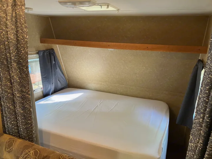 Clean RV rental sleeping area featuring a bed, window, curtains, and built-in shelf.. Gulf Stream Ameri-Lite 25 BS 2008