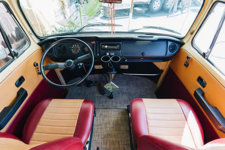 Inside a vintage VW camper RV rental, showcasing the dashboard, steering wheel, and two-tone front seats.. Volkswagen Westfalia 1978