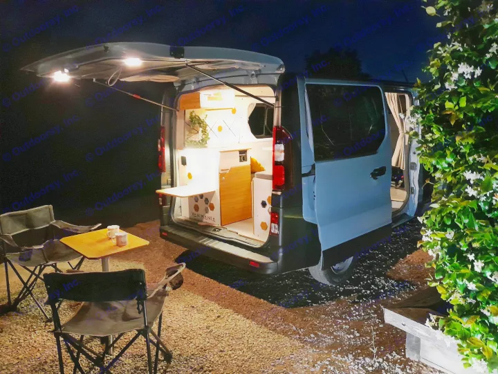 Experience RV rental! A light blue camper van with its illuminated, modern interior open at night, set up for cozy outdoor camping.. Renault Traifc + aménagement NW Van Mania 2019