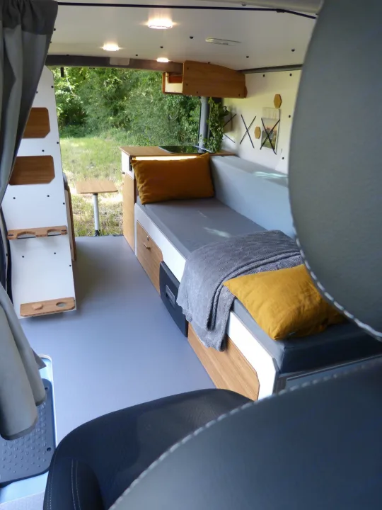 Step into this cozy RV rental's modern interior. Custom wood & gray design with bed, kitchen, and smart storage for travel.. Renault Traifc + aménagement NW Van Mania 2019