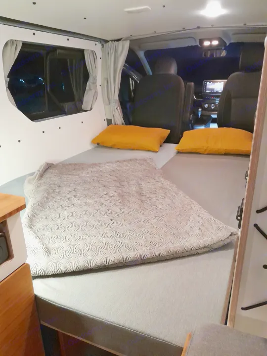 Inside a cozy rv rental: A comfortable bed with bright yellow pillows & grey blanket is ready for a good night's sleep.. Renault Traifc + aménagement NW Van Mania 2019