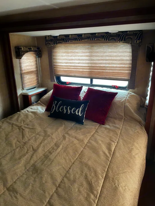 Cozy RV rental bedroom with a comfy bed, decorative pillows, and pleated blinds, offering a comfortable travel stay.. Forest River Sunseeker 2016