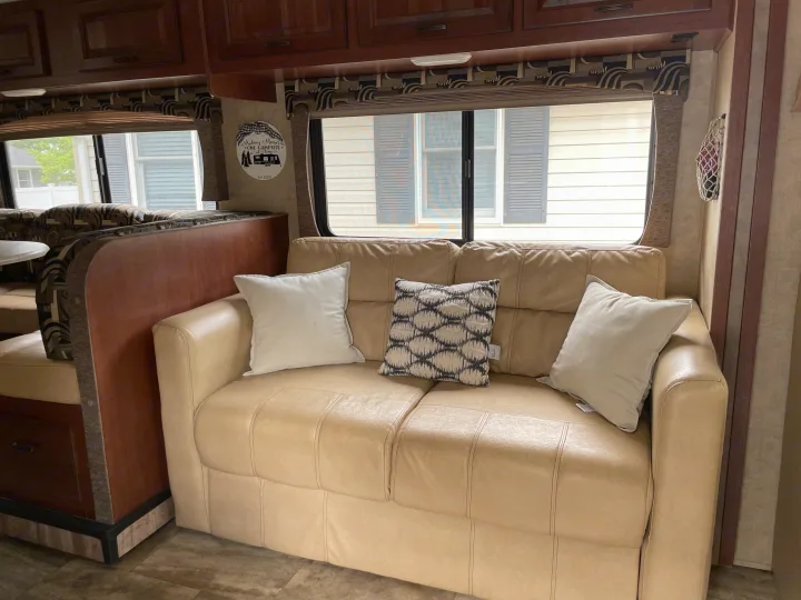 Cozy RV rental interior with a light sofa, decorative pillows, and a dining booth, ideal for travel adventures.. Forest River Sunseeker 2016
