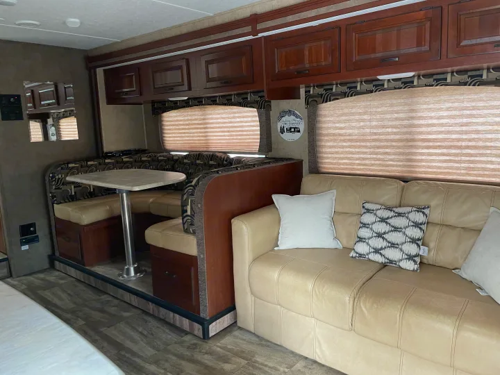Cozy RV rental interior showcasing a dinette with bench seating, a cream sofa with pillows, and wood-toned cabinets.. Forest River Sunseeker 2016