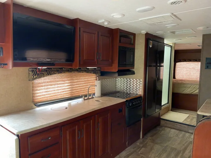 RV rental interior: kitchen with sink, stove, microwave, and fridge; wall-mounted TV; and cozy bedroom area.. Forest River Sunseeker 2016