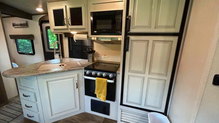 RV rental kitchen: light cabinets, gray counter, black appliances (sink, stove, microwave, fridge) for comfortable travel.. Keystone Cougar Half-ton 2022