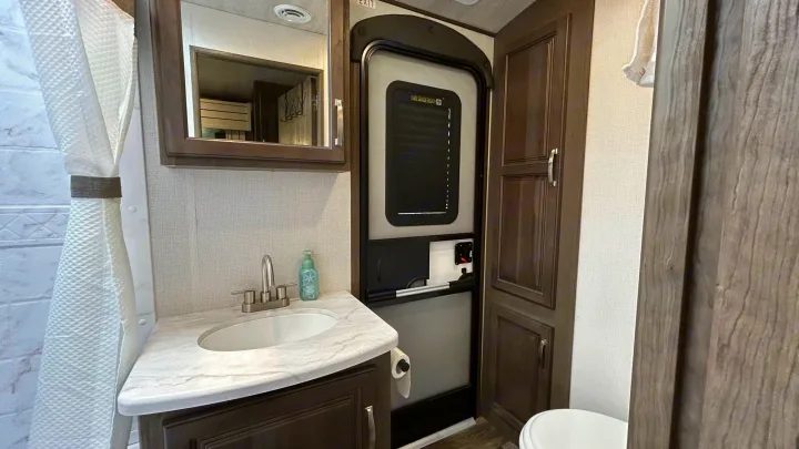 RV rental bathroom: features a vanity with sink, mirror, shower, and toilet, plus the main entry door visible.. Keystone Cougar Half-ton 2022