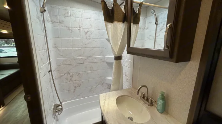 Clean, compact bathroom in an RV rental, featuring a shower/tub combo and vanity with a sink.. Keystone Cougar Half-ton 2022