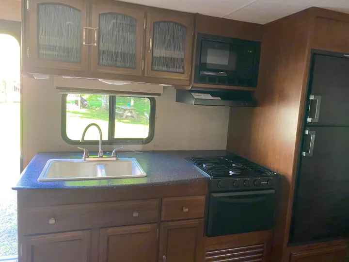 RV rental kitchen: view of sink, stove, microwave, fridge & cabinets, looking out a window.. Coachmen Freedom Express 2020