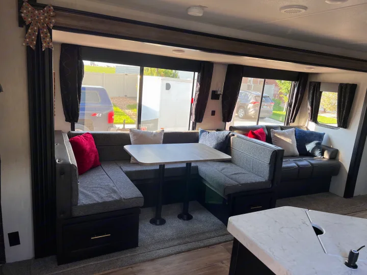 Spacious RV rental interior with U-shaped dinette seating, table, & pillows. Large windows offer outdoor views for travel comfort.. Forest River Cherokee 2022